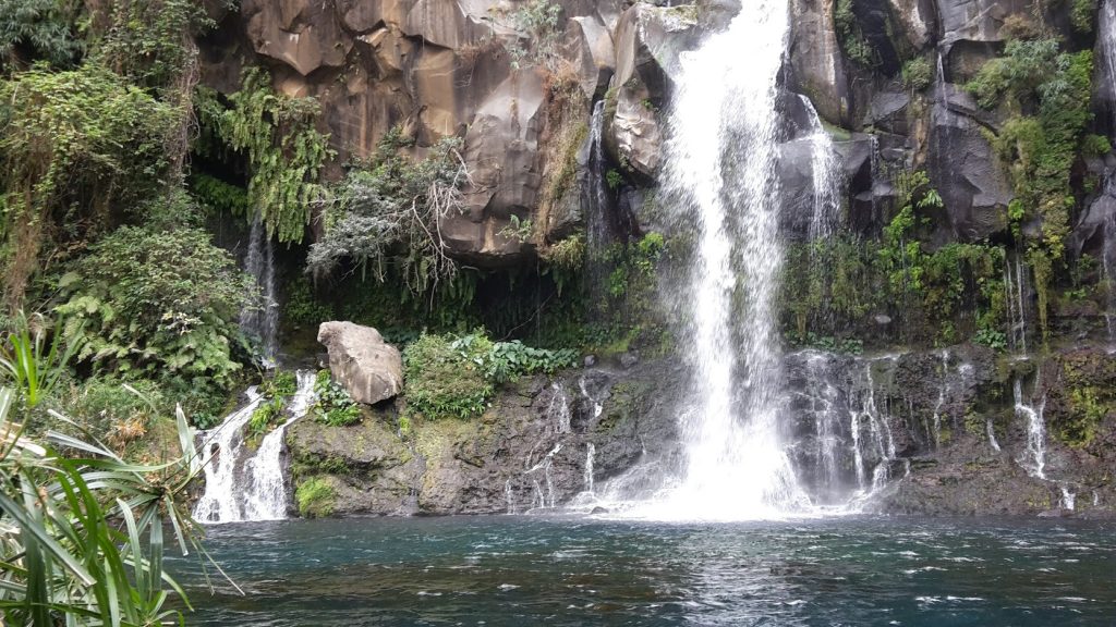 Cascade d’eau se déversant dans un bassin naturel, entourée de rochers et d’une végétation verdoyante.